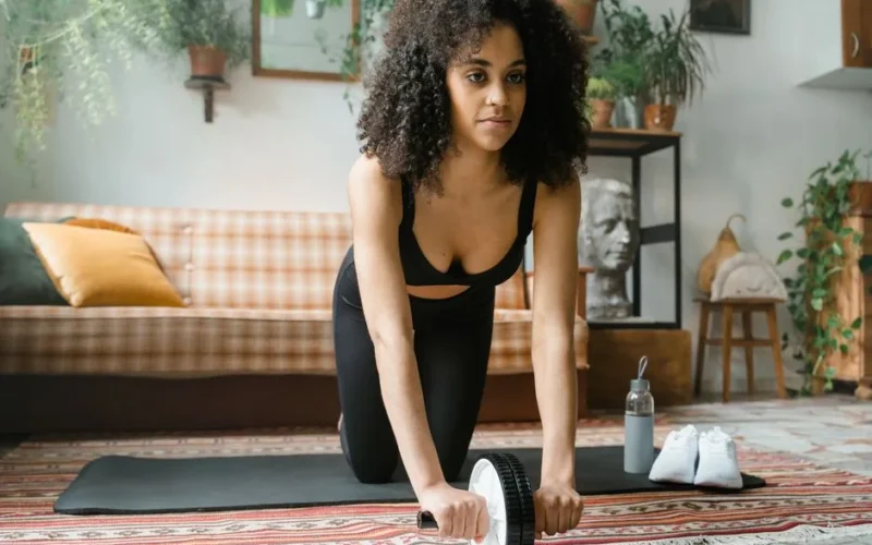 Woman in activewear using ab wheel for exercise in a stylish living room.