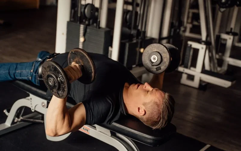 A man exercises with dumbbells on a bench press at a gym, focusing on fitness and strength.