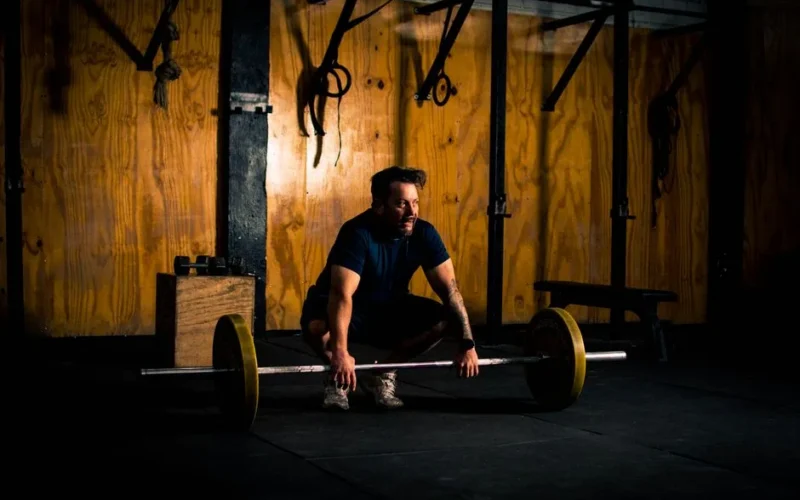A man prepares to lift a barbell in a dimly lit gym environment, focusing on strength training.