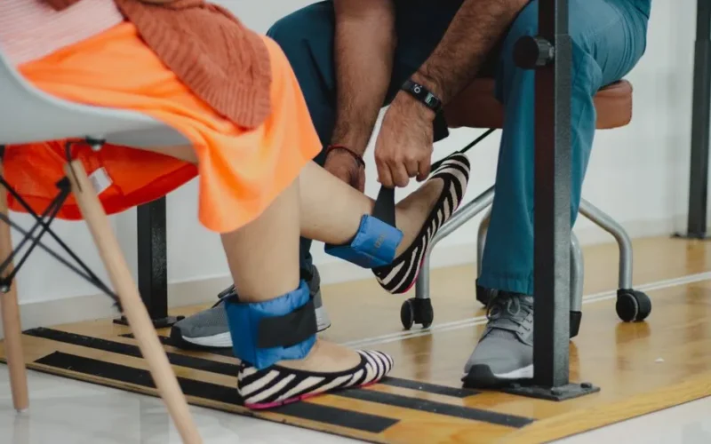 A therapist assists a woman during a rehabilitation session involving ankle weights.