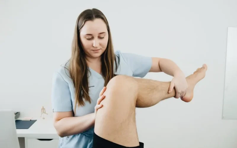 A physiotherapist assisting a patient's leg therapy session indoors, focusing on rehabilitation.