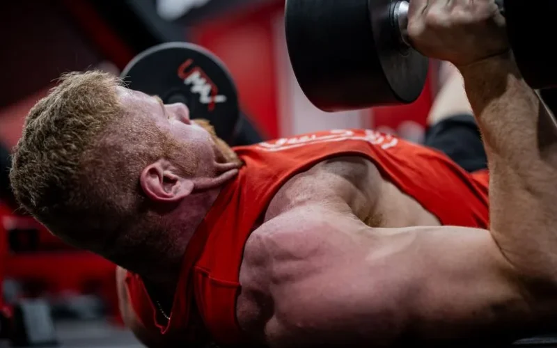 Muscular man performing a dumbbell press workout, focusing on strength and endurance.