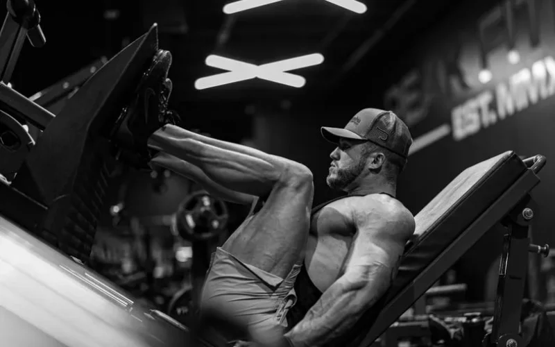 Strong muscular man performing leg press exercise in a modern gym setting.