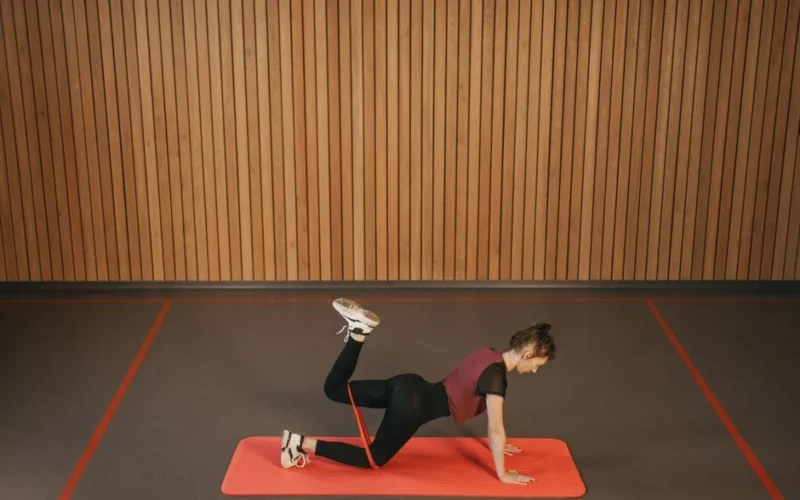 Woman performing a resistance band workout on a mat indoors, focusing on fitness and strength.