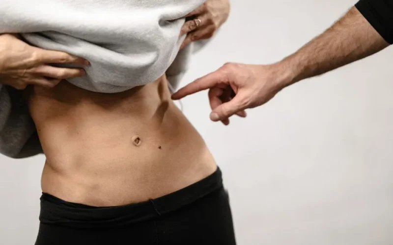 An intimate close-up of a person's toned abdominal area with a hand pointing, emphasizing fitness.