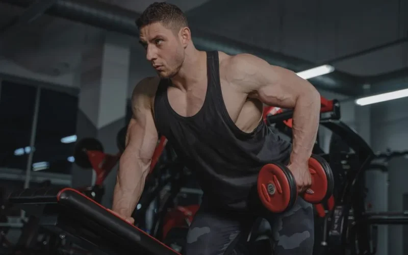 Strong male bodybuilder lifting dumbbells in a gym environment.