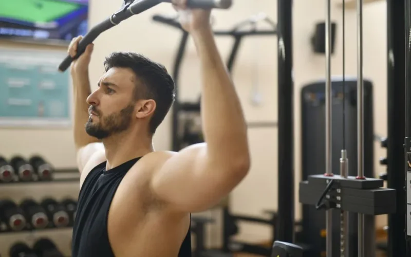 Man performing strength exercise on lat pulldown machine in gym.