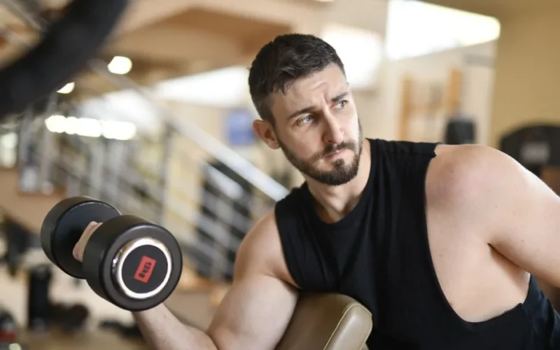 A determined man lifting a dumbbell indoors, showcasing strength and fitness.