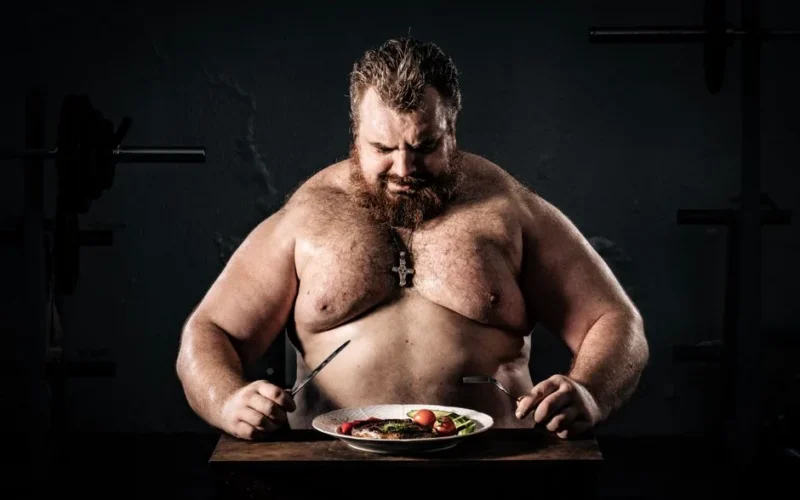 Shirtless muscular man eating a nutritious meal, symbolizing strength and health.
