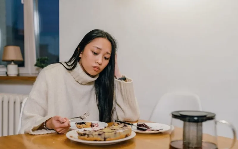 A thoughtful woman in a cozy sweater eats dessert alone, reflecting deep thoughts.