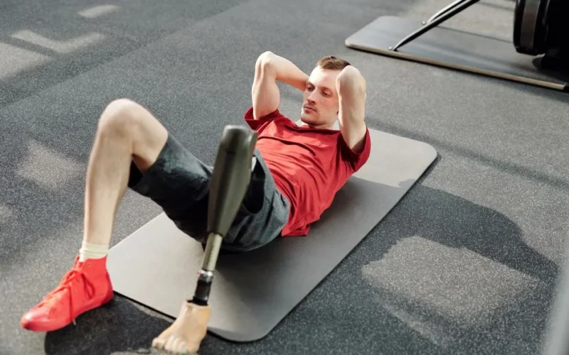 Man performing sit-ups on yoga mat using prosthetic leg in fitness gym.