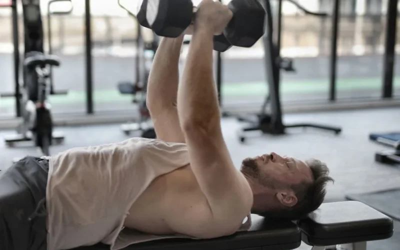 Man performing dumbbell press on bench indoors, focusing on muscle strength.