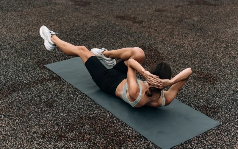 Fit woman doing a bicycle crunch on a mat outdoors, emphasizing core strength and fitness.