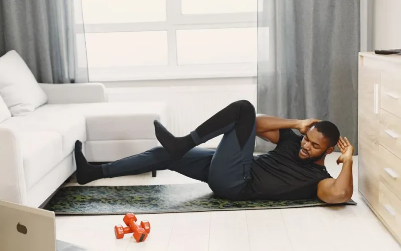 A black man performing abdominal exercises on a yoga mat at home.