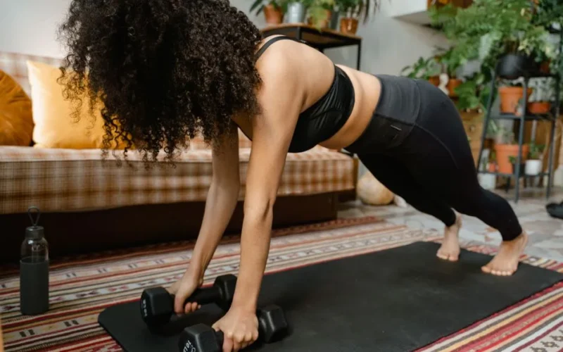 Woman performing push-ups with dumbbells on yoga mat in cozy indoor setting.