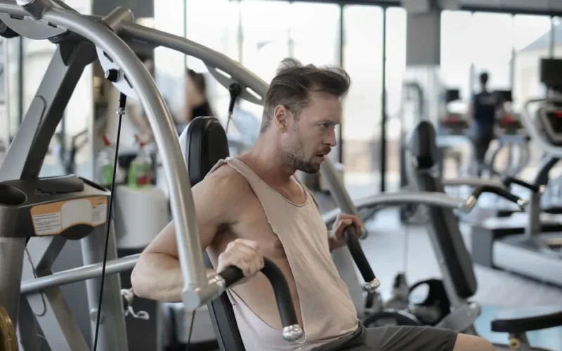 Side view of determined athletic male in sportswear pumping muscles during workout in fitness center and using shoulder press machine