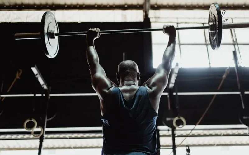Man lifting barbell in gym from back view highlighting strength and fitness.