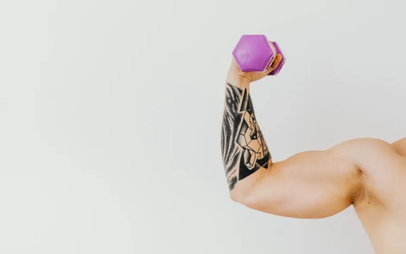 A tattooed arm lifting a purple dumbbell, showcasing strength and fitness.