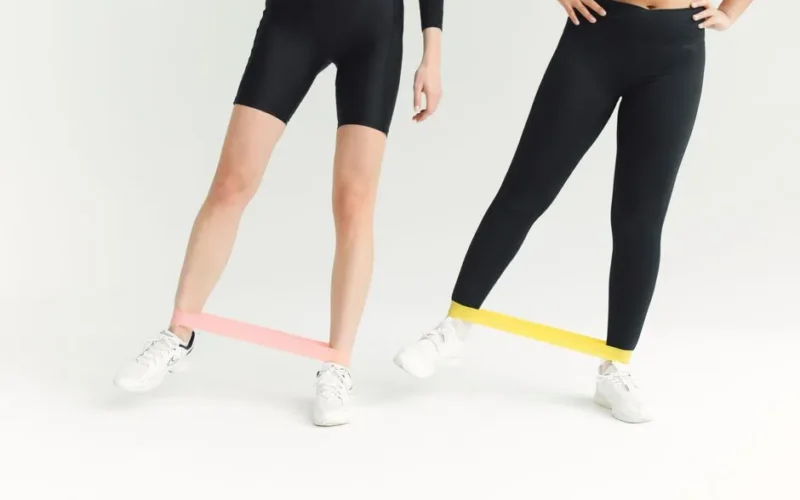 Two women exercising with resistance bands, focusing on leg workouts in a minimalistic setting.