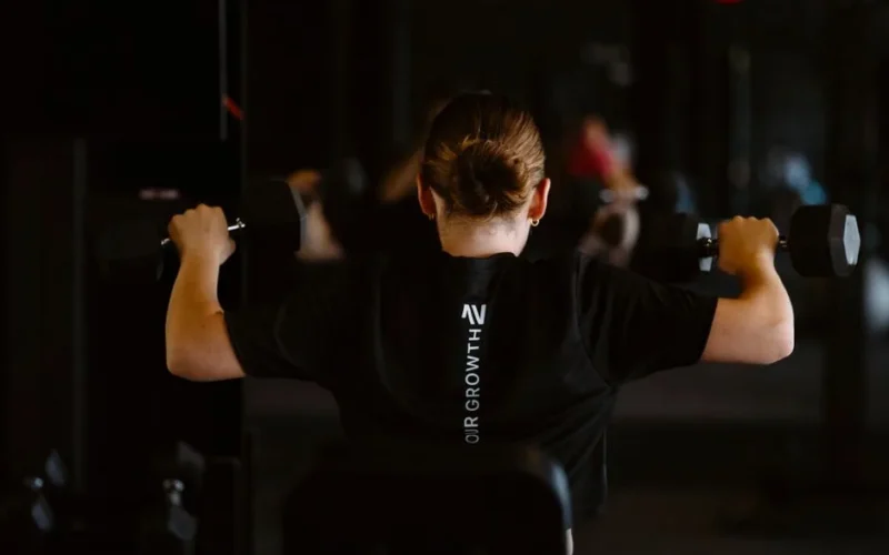 Woman working out with dumbbells in a gym setting. Rear view capturing strength and focus.
