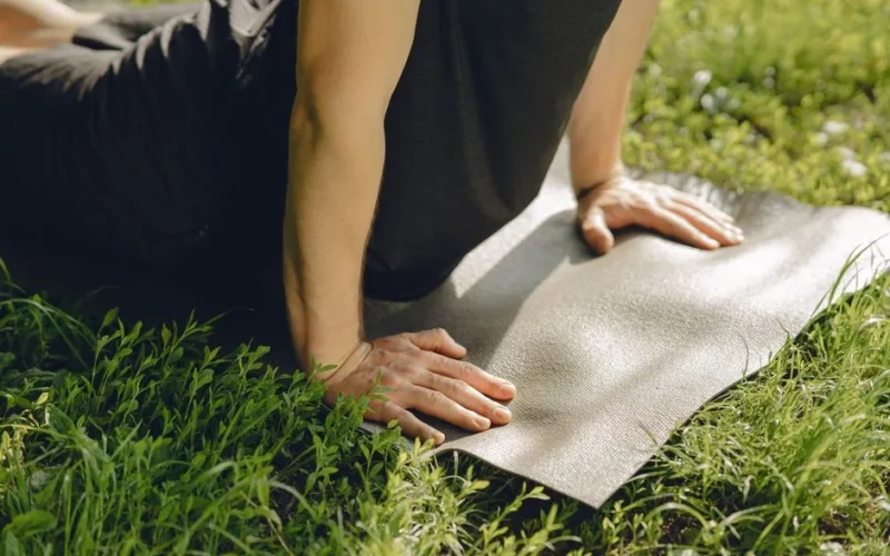 Man practicing yoga outside on a mat in a sunny park.