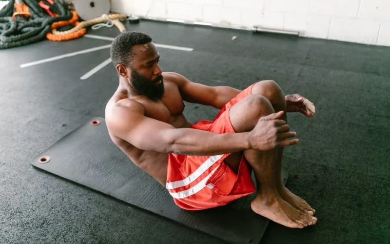 A physically fit man doing sit-ups on a mat indoors, focusing on core strength.