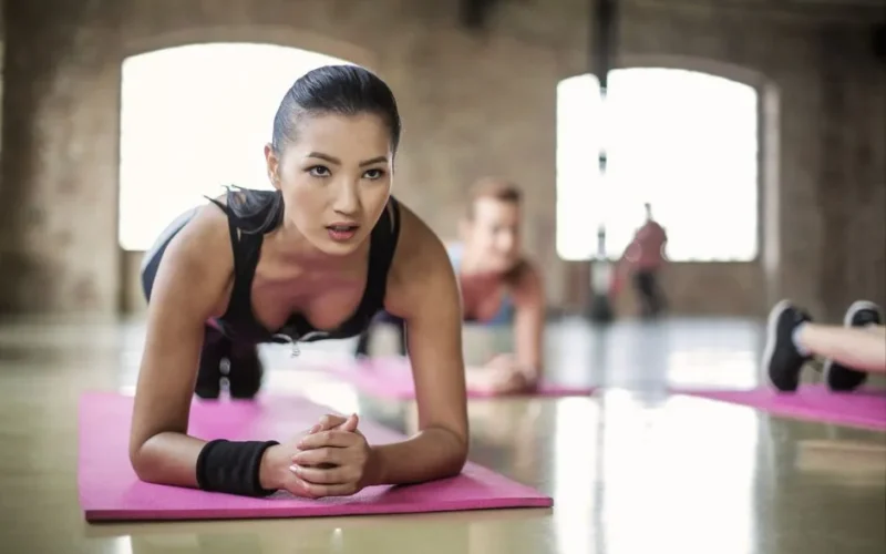 Two women engaging in a focused yoga session on pink mats in a spacious indoor studio.