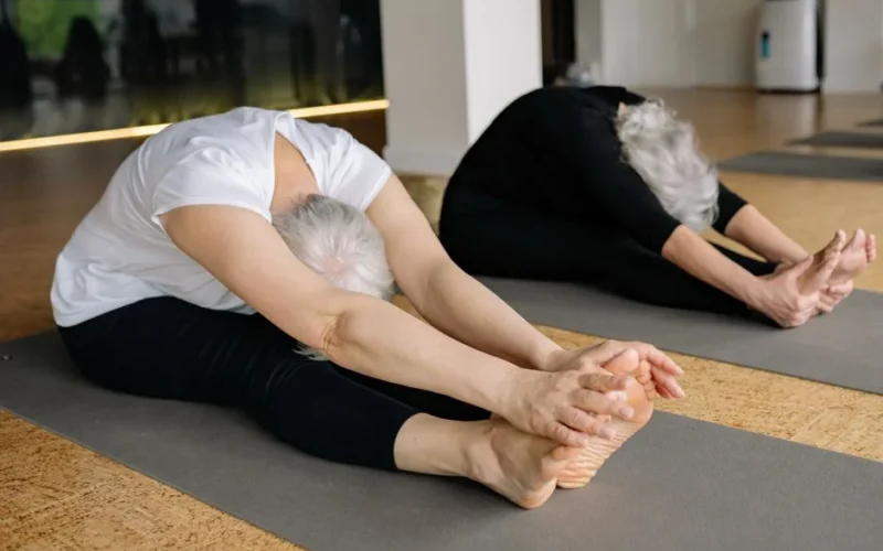 Two senior women engaging in yoga stretches indoors, promoting healthy lifestyle and flexibility.