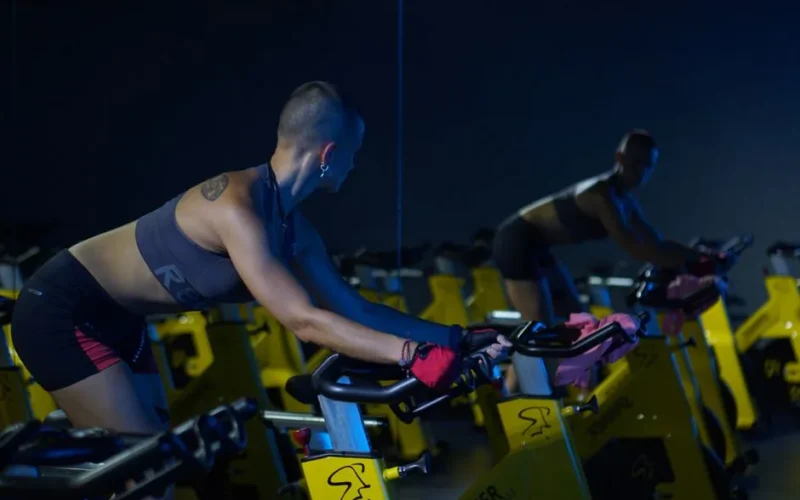 A woman exercising on a stationary bike in a dimly lit gym, focused on fitness and endurance.