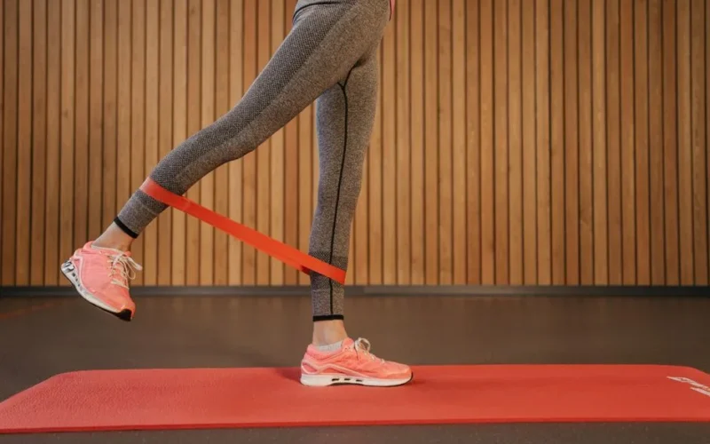 A woman performing leg exercises using a red resistance band on a yoga mat indoors.