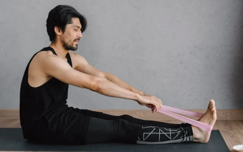 Adult man performing stretching exercises with a resistance band on a yoga mat indoors for fitness and wellness.