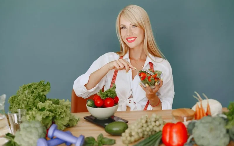 Blonde woman enjoying a fresh salad surrounded by vegetables, promoting healthy eating.