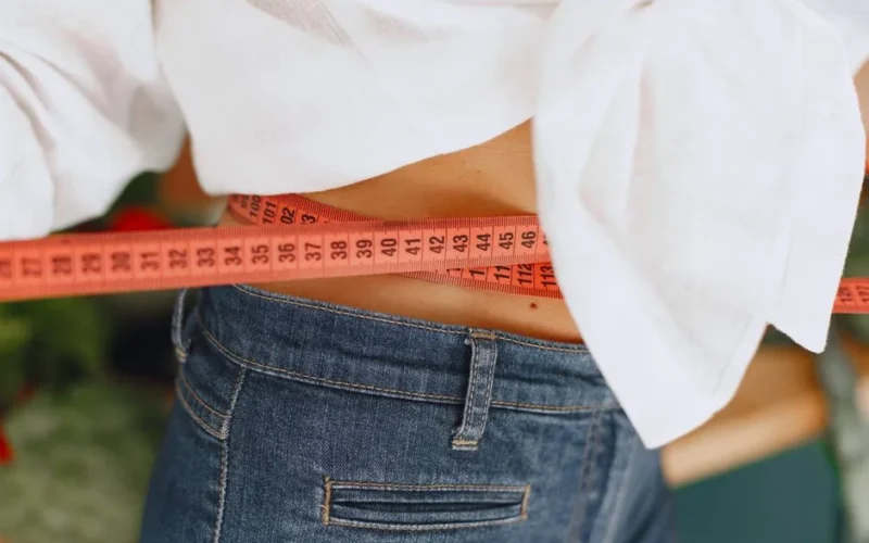 Close-up image of a woman measuring her waist with a tape measure, promoting fitness and health goals.