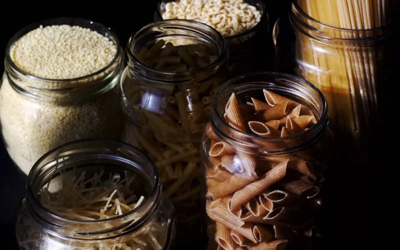 Different types of pastas and cereals in glass jars on kitchen in sunlight