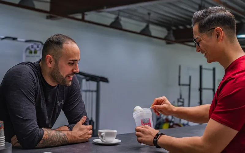 Side view of strong friends talking while preparing high protein smoothie after hard workout