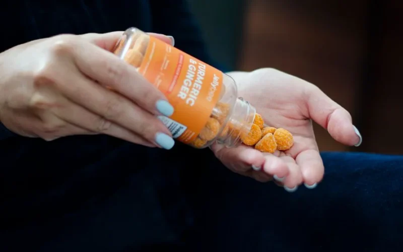 Close-up of a woman holding turmeric ginger gummies in hand, promoting a health supplement.