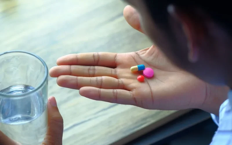 A hand holding a variety of pills alongside a glass of water, emphasizing health and medication.