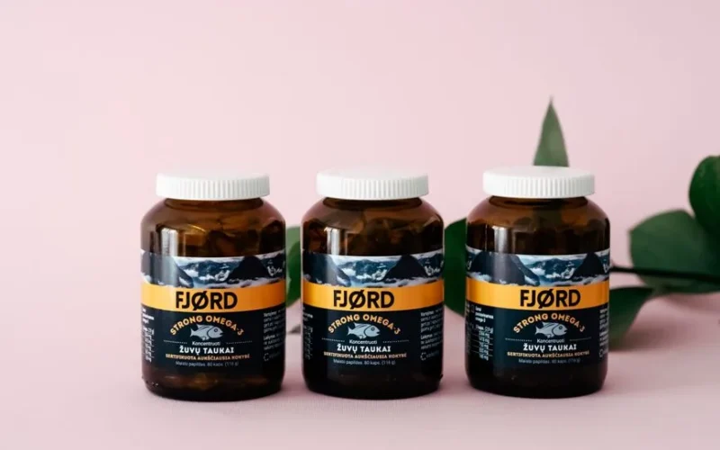 Three FJORD Omega-3 supplement bottles on a pink backdrop with greenery accents.