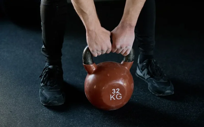 A person lifting a 32 kg kettlebell in a gym setting, showcasing strength training.