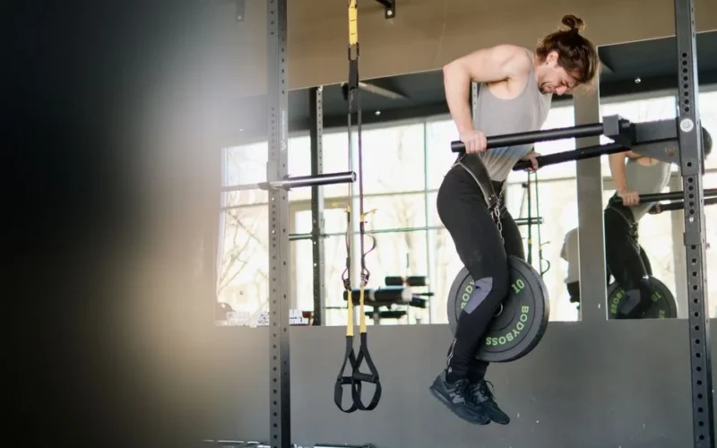 Fit man performing weighted pull-ups in a gym setting, showing strength and determination.