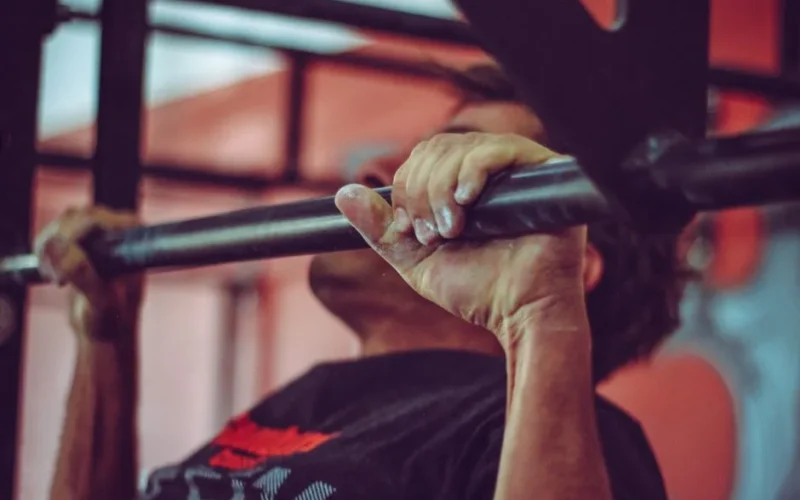 Focused shot of a man doing pull-ups in a gym, highlighting his strength and endurance.