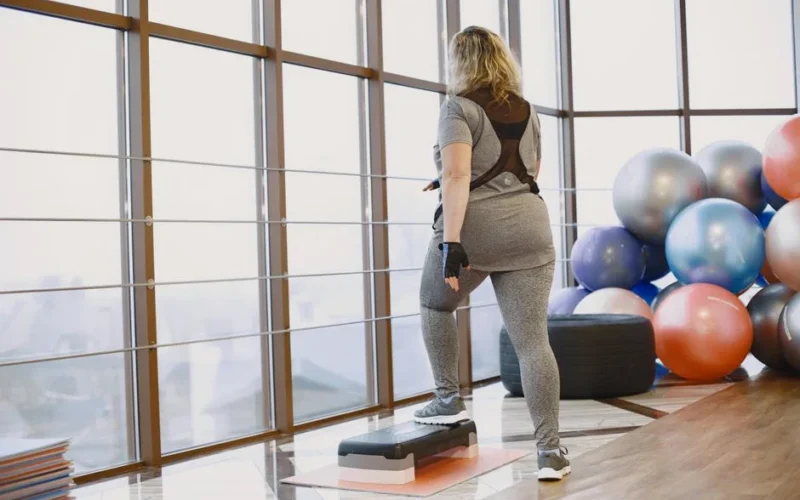 Back view of a woman exercising indoors with fitness equipment and step platform.