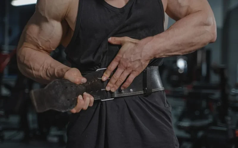 Close-up of a muscular man adjusting a weightlifting belt in a gym setting.