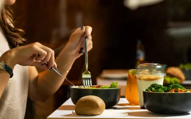 A woman dining on a fresh salad with vegetables and a drink indoors.