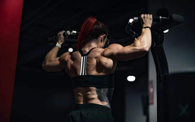 Back view of a muscular woman lifting weights in a gym, showcasing strength and determination.