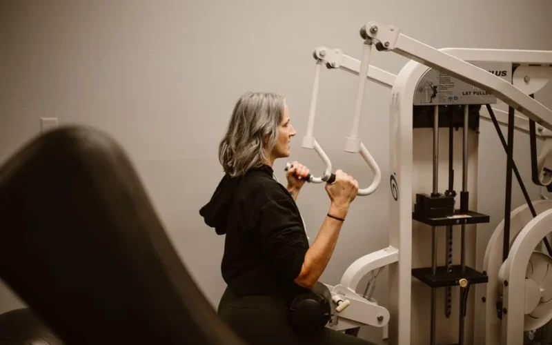 A middle-aged woman with gray hair using a lat pulldown machine for fitness indoors.