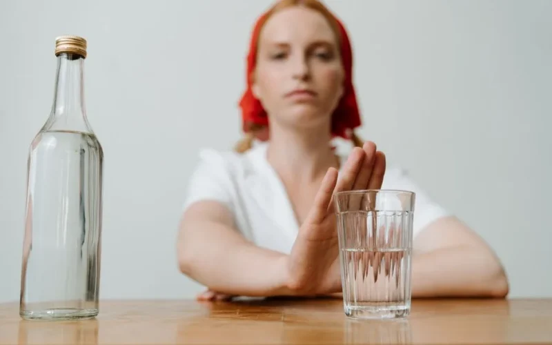 A woman with a red kerchief rejects a glass of alcohol, symbolizing sobriety or refusal.