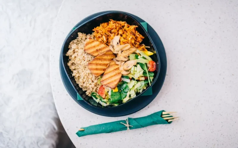 A nutritious bowl featuring grilled tofu, quinoa, fresh salad, and mushrooms on a light background.