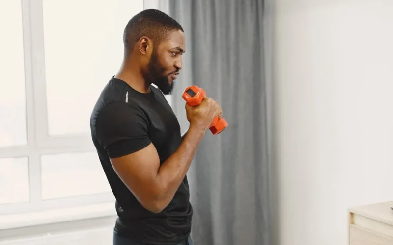 African American man exercising with a dumbbell indoors. Fitness and healthy lifestyle concept.