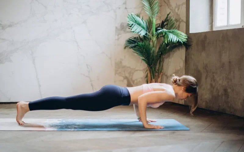 Woman in active wear doing yoga push-up on mat indoors, embracing healthy lifestyle.